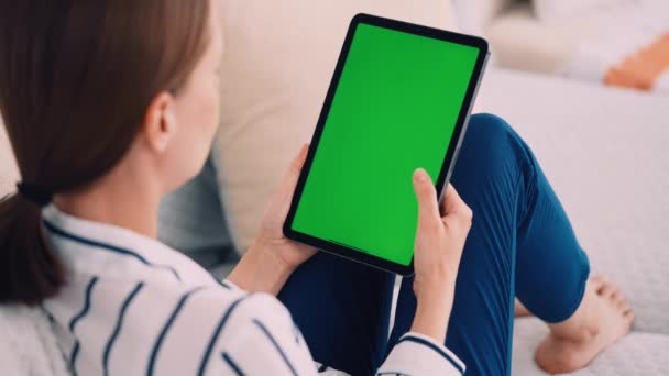 woman sitting on the sofa holding digital tablet vertical scrolling green screen display weekend at home - Video, Çekim