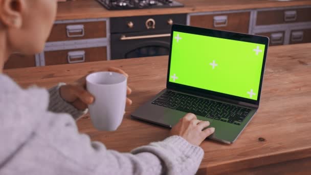 woman using Touchpad for Scrolling the Web holding cup with tea laptop on kitchen table working at home - Materiał filmowy, wideo