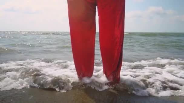 Santa Claus in suit stands on beach or ocean. Exotic Christmas meeting on island on beach with sand in hot weather. Waves, sea. Time to relax on vacation. legs close-up. slow motion - Filmagem, Vídeo