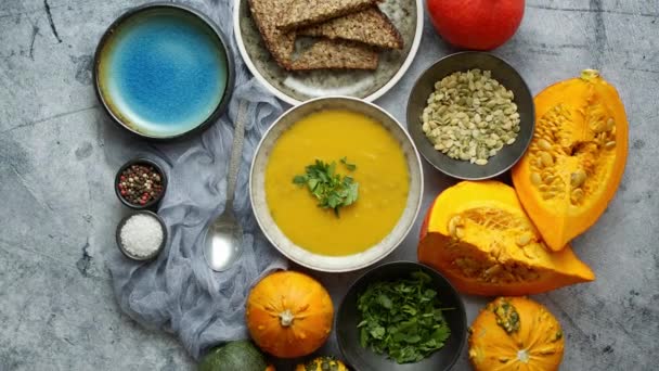 Traditional fall and winter dishes, hot and spicy pumpkin soup with pearsley, seeds and freshly baked bread, on stone table, flat lay top view - Filmagem, Vídeo