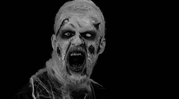 Hombre aterrador con Halloween zombie maquillaje herido sangriento, tratando de asustar, expresiones de la cara. Tema Horror. Un siniestro no-muerto aislado en un estudio de fondo negro. Rituales de vudú. Arte corporal de moda - Foto, Imagen