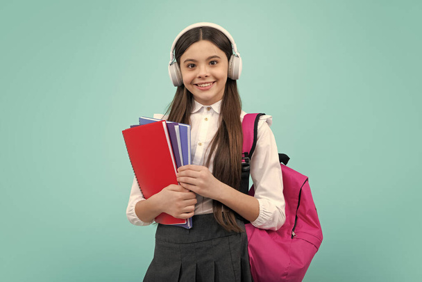 Schoolmeisje, tiener student lifestyle meisje in hoofdtelefoon houden boeken over blauwe geïsoleerde studio achtergrond. School- en muziekonderwijs - Foto, afbeelding