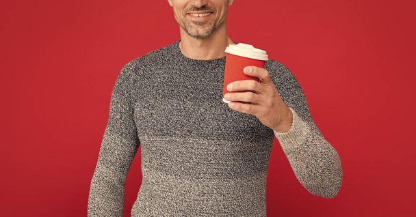 um homem cansado a beber café. modelo de moda masculina segurar copo. moda de inverno. Café da manhã. feliz cara grisalho em suéter no fundo vermelho. - Foto, Imagem