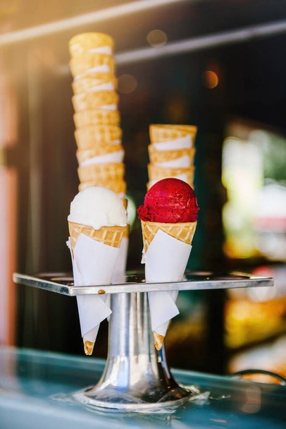 White vanilla and red cherry ice cream cones in metal hygienic holder on counter at store one red scoop of strawberry ice cream and another white yoghurt one - Φωτογραφία, εικόνα