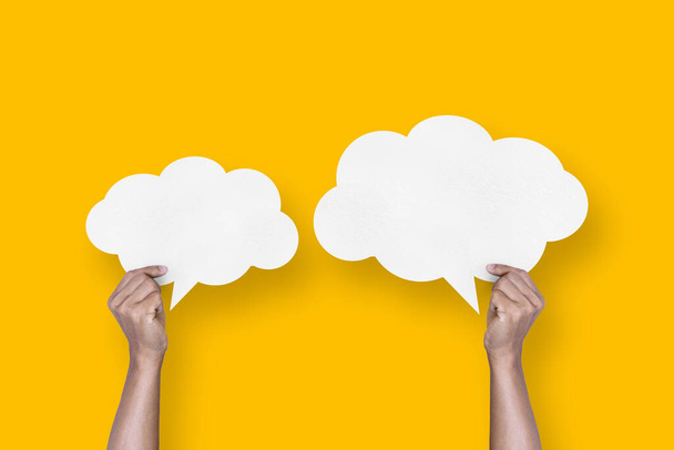 hand holding white paper cloud shape speech bubble balloon isolated on yellow background communication bubbles. - Foto, Imagem
