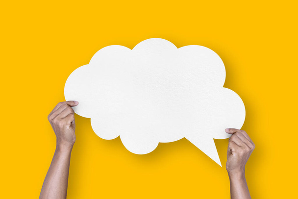 hand holding white paper cloud shape speech bubble balloon isolated on yellow background communication bubbles. - 写真・画像