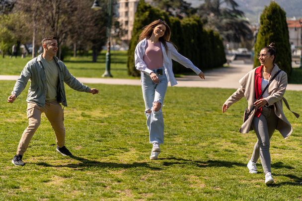 Счастливая молодая группа студентов, гуляющих вместе и веселящихся на зеленой лужайке - Фото, изображение