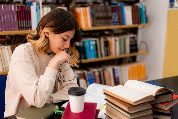 Hermosa chica estudiando en un escritorio en una biblioteca - Foto, Imagen