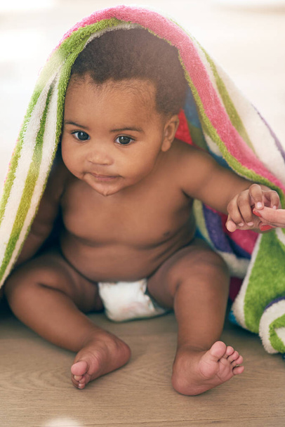Somebody get me outta here. an adorable baby girl covered in a colorful blanket at home - Foto, Bild