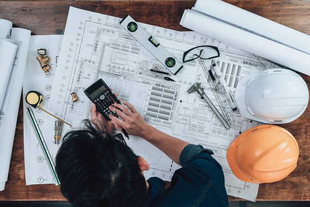 Top view Engineering working with drawings inspection and press calculator on the office desk and triangle ruler, safety glasses, compass, vernier caliper on Blueprint. Engineer, Architect, Industry and factory concept. - Foto, Imagen