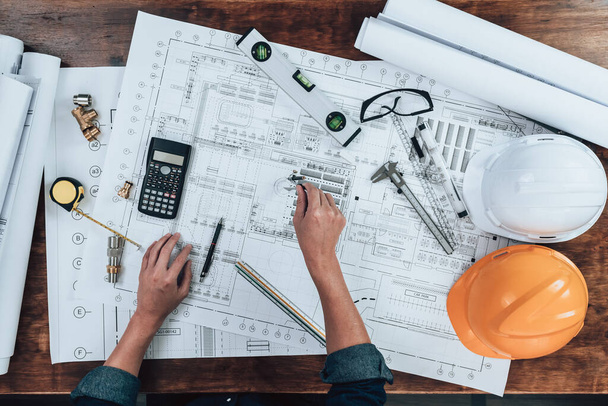 Top view Engineering working with drawings inspection and writing on the office desk and Calculator, triangle ruler, safety glasses, compass, vernier caliper on Blueprint. Engineer, Architect, Industry and factory concept. - Photo, image