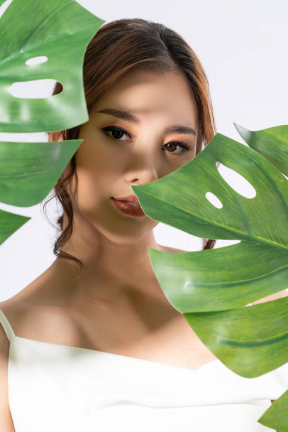 Closeup portrait of young gorgeous woman with healthy fair skin holding big green leaf near her face. Skin care beauty care concept. - Photo, Image