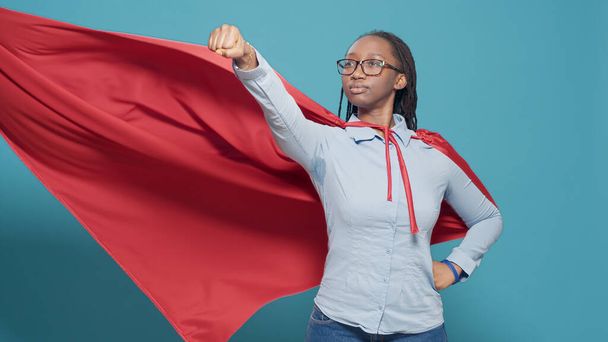 Portrait of superhero with flying red cape on camera, posing as action cartoon character with costume and cloak. Showing motivation and strength in studio, positive and powerful. - Fotó, kép