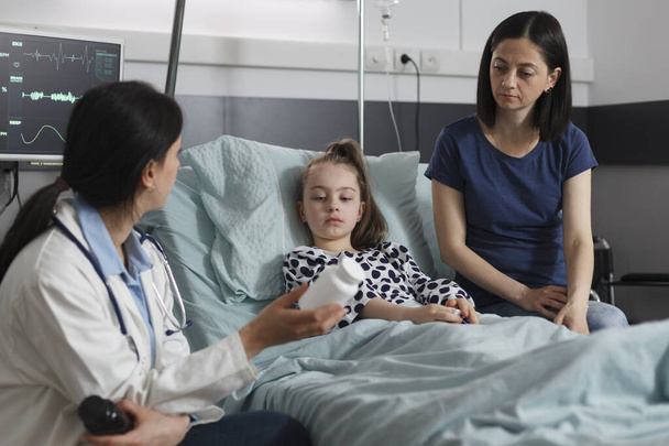 Expert pediatrician prescribing medication for little girl disease resting in patient bed. Doctor expert recommending antibiotics for ill kid sickness hospitalized in children healthcare facility. - Valokuva, kuva