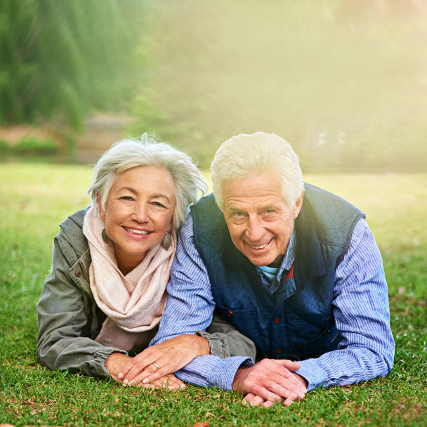 Living the retirement dream. Portrait of a happy senior couple lying down on the grass together in the park - Photo, image