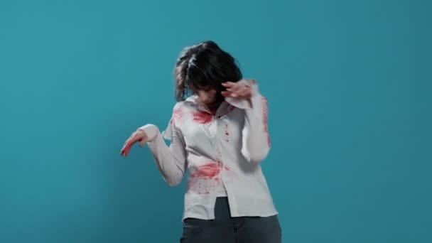Mindless and scary zombie dancing on blue background. Evil frightening brainless aggressive monster with deep and bloody wounds and scars having fun while dancing in front of camera. - Materiał filmowy, wideo