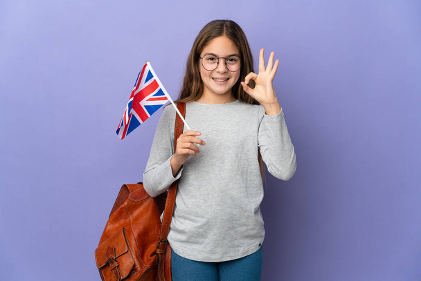 Dziecko trzymające flagę Zjednoczonego Królestwa na odosobnionym tle pokazującym znak ok palcami - Zdjęcie, obraz