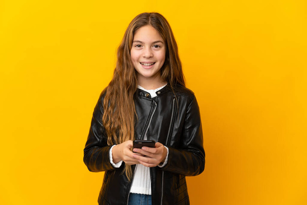 Child over isolated yellow background sending a message with the mobile - Foto, imagen