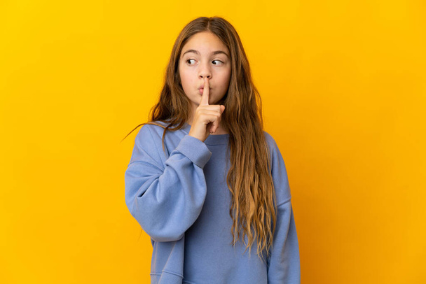 Child over isolated yellow background showing a sign of silence gesture putting finger in mouth - Foto, imagen