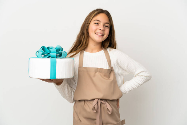 Klein meisje met een grote taart over geïsoleerde witte achtergrond poseren met armen op heup en glimlachen - Foto, afbeelding