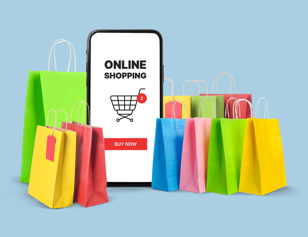 Big smartphone with text ONLINE SHOPPING on screen and many paper bags on blue background - Photo, image