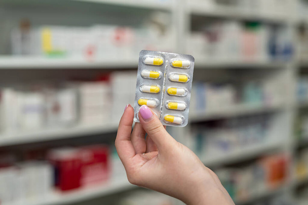 Mano del farmacista tenendo molte pillole diverse vicino al petto sullo sfondo di scaffali con farmaci. Il concetto di farmaci al farmacista - Foto, immagini
