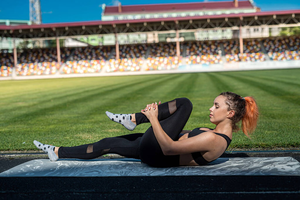 Deportiva joven atleta estirando las piernas en el estadio universitario, estilo de vida saludable   - Foto, Imagen