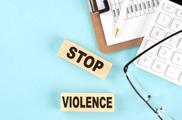STOP VIOLENCE texte écrit sur un bloc de bois avec presse-papiers, lunettes et calculatrice - Photo, image