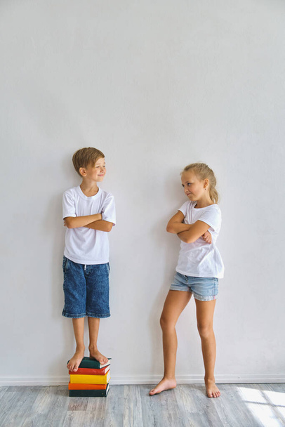 クールな子供たち、小さな男の子と女の子は彼らの高さを測定し、比較し、白い壁の近くに楽しみを持っている - 写真・画像