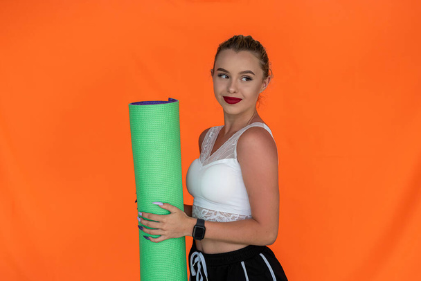 Sporty woman goes to yoga class holding a fitness mat for class on a plain background. Fitness mat in the hands of a woman. Woman in the background. Health concept - Photo, image