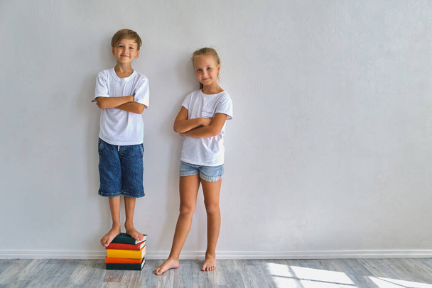 Cool kids, little boy and girl measure their height and compare, have fun near white wall - Photo, Image