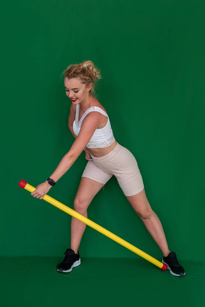 una chica joven con un cuerpo atlético hace un ejercicio de fitness con un palo de fitness en el fondo. Concepto de chica deportiva - Foto, imagen