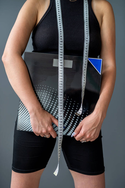 Eine junge Frau hält ein Maßband als Symbol für Ernährung und eine Waage zur Messung des Körpergewichts in der Hand. Gesundheitskonzept. Körper isoliert auf grauem Hintergrund. Ernährung - Foto, Bild