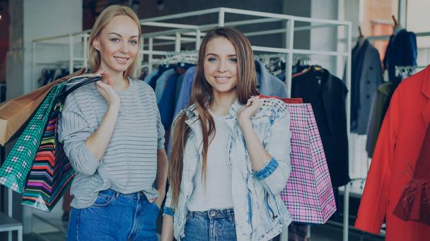 Portrait of beautiful young women are standing with lots of paper bags in their hands in luxurious womens clothes boutique. Fashionable clothes, bags, shoes and baloons in background. - Foto, Bild