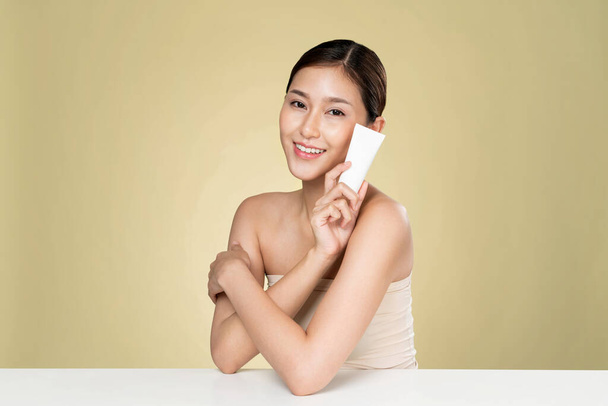 Ardent woman smiling holding mockup product for advertising text place, light grey background. Concept of healthcare for skin, beauty care product for advertising. - Foto, afbeelding