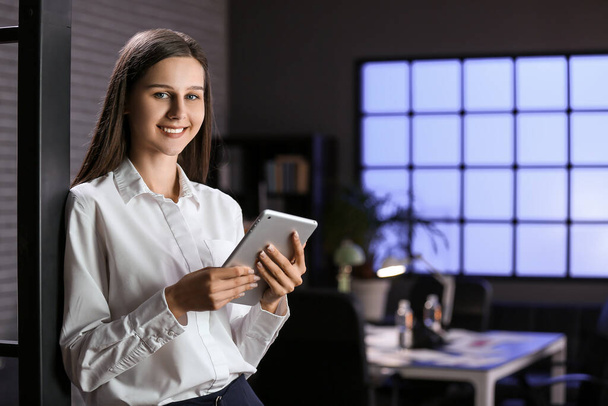 Smiling businesswoman working with tablet computer in office at night - 写真・画像
