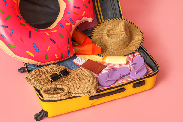 Open suitcase with clothes, beach accessories and passport on pink background, closeup - Foto, Imagen