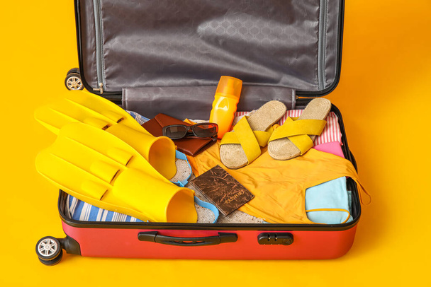 Open suitcase with beach accessories and passport on yellow background - Фото, изображение