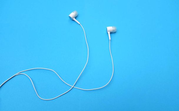 white music headphones ,earphones with headset on isolated bright blue background. Music concept. Top view - 写真・画像