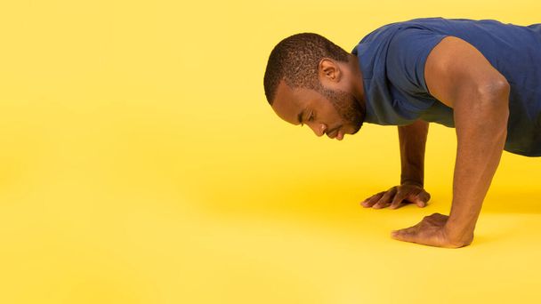 Sporty African American Man Doing Push Ups Exercising Flexing Muscles Over Yellow Studio Background. Fitness Workout Concept. Side View, Panorama With Empty Space - Photo, image
