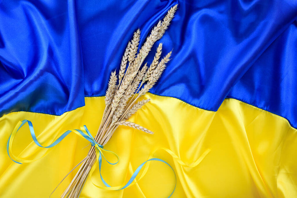 Bundle of wheat spikes with yellow and blue ribbon on the background of the flag of Ukraine. Harvest of wheat and concept of Ukraine. Flat lay, copy space - Fotó, kép