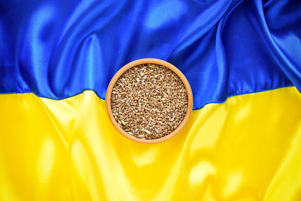 Bowl with wheat grains on the background of the flag of Ukraine. Concept of food supply crisis and global food scarcity because of war in Ukraine. - Zdjęcie, obraz