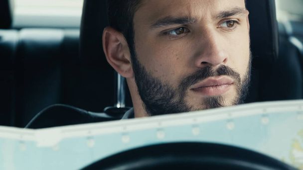 portrait of bearded man sitting in automobile with map - Фото, изображение