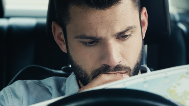 pensive man looking at map while sitting in car and estimating route - Foto, imagen