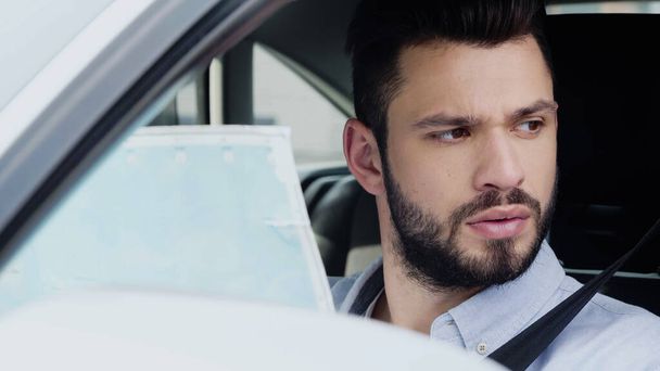 young bearded man looking away while sitting in car with map - Fotó, kép