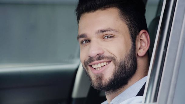 portrait of happy young man driving car and smiling at camera - Фото, изображение