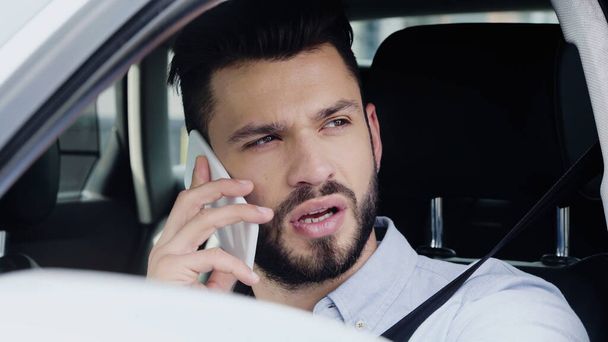 young bearded man driving car while looking away and talking on smartphone - Fotoğraf, Görsel