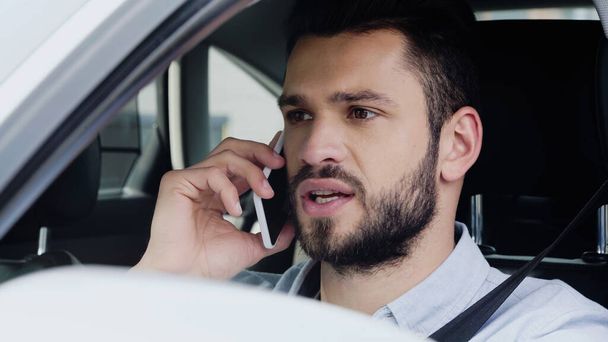 молодий чоловік дивиться вперед і розмовляє по мобільному телефону під час водіння автомобіля
 - Фото, зображення