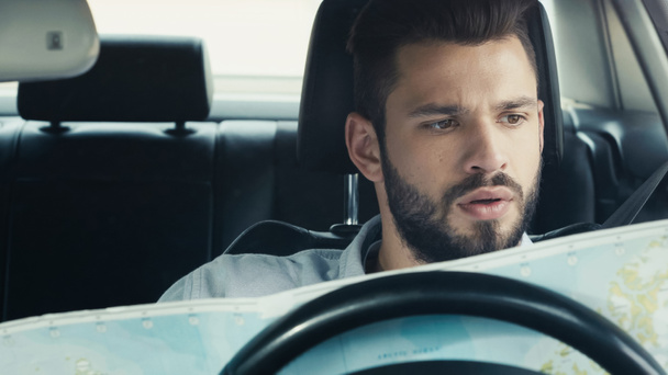 thoughtful bearded man looking at map while sitting in car - Foto, Imagen
