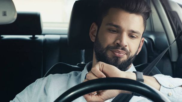 displeased bearded man driving car and looking at wristwatch - Fotografie, Obrázek